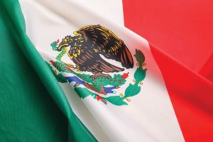 A MEXICAN FLAG STRIPED GREEN, WHITE AND RED SPORTS AN INSIGNIA AT THE CENTER DEPICTING AN EAGLE WITH A SERPENT IN ITS BEAK.